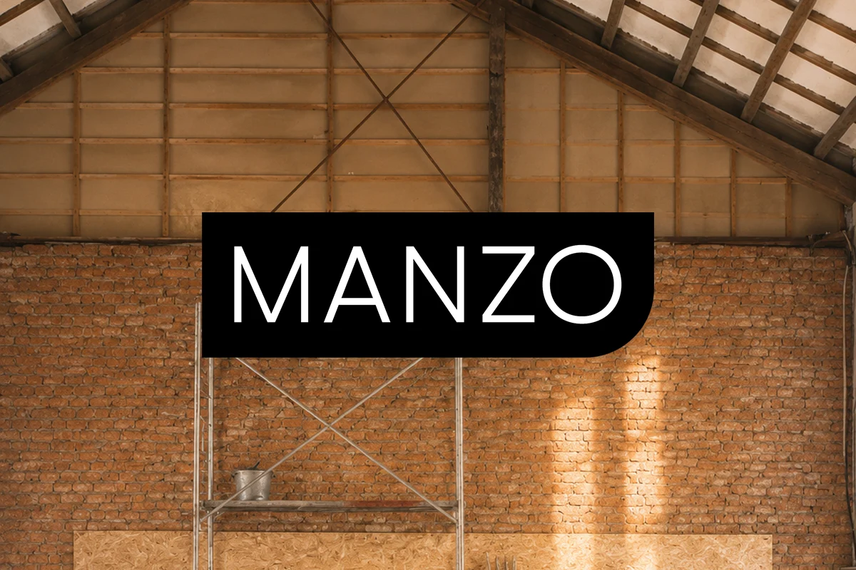 MANZO wordmark displayed in a brick-walled furniture workshop